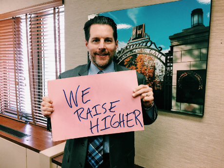 peter holding up we raise higher sign