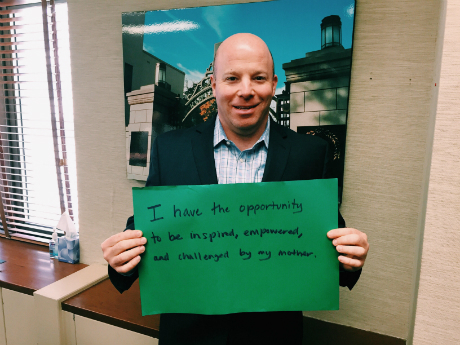 robert holding up a sign that reads i have the opportunity to be inspired, empowered, and challenged by my mother